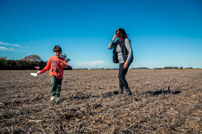 Grandmother with grandson walking on land against blue sky