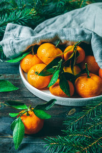 Tangerines with green leaves on a green wooden table in a rustic style surrounded by spruce branches