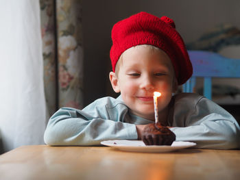 Little boy looking at birthday cake with glowing candle at home.