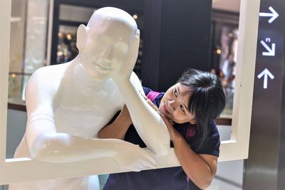 Smiling young woman looking at statue while standing in shopping mall