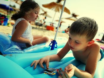 Brother and sister sitting on inflatables at shore of beach