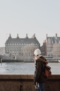 Rear view of woman looking at river in city against sky