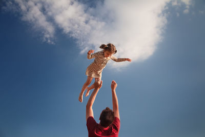 Low angle view of father tossing daughter mid air against sky
