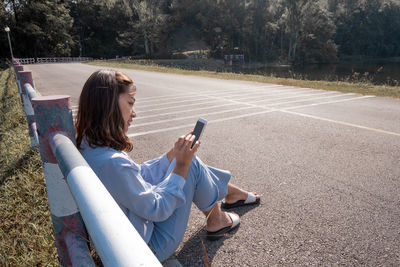 Woman using mobile phone while sitting on road