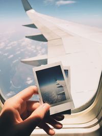 Cropped hand holding picture frame against airplane window