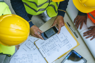 Woman and two men in workwear taking cell phone picture of a construction plan