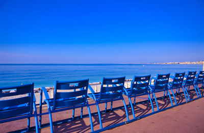 Empty chairs on beach against clear blue sky