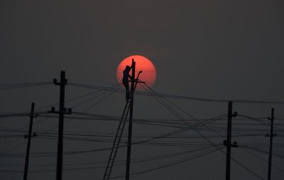 Low angle view of silhouette electricity pylon against sky during sunset