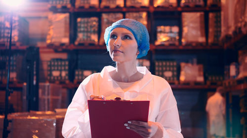 Young woman looking away while standing against illuminated built structure