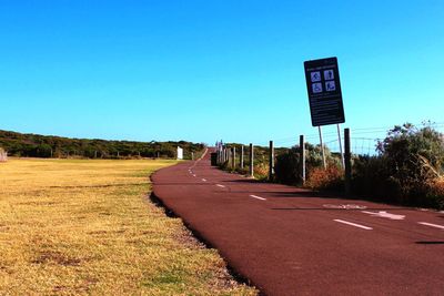 Road sign on road against clear blue sky