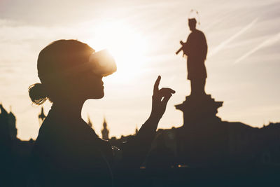 Silhouette woman standing against statue during sunset