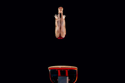 Low angle view of female gymnast jumping against black background