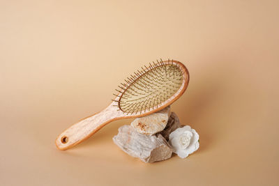 Close-up of a wooden hair brush on stone podium with flower on beige background