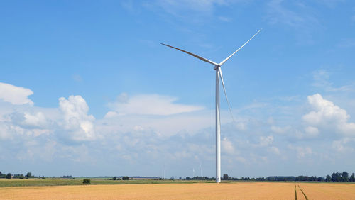 Wind turbines on field against blue sky during sunny day