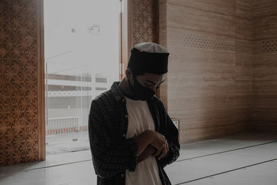 Man wearing hat standing against wall at home