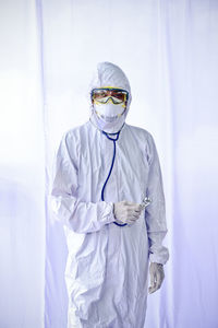 Portrait of doctor wearing protective suit standing against white background