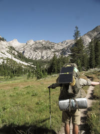 Rear view of hiker with backpack on grassy field against mountain