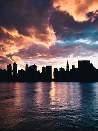 Silhouette buildings by sea against sky during sunset