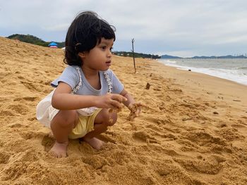Boy sitting on sand at beach against sky