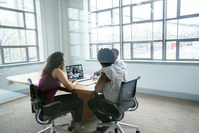 Business people discussing with businesswoman over video conference in board room seen through glass