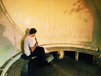 Side view of young man sitting against wall