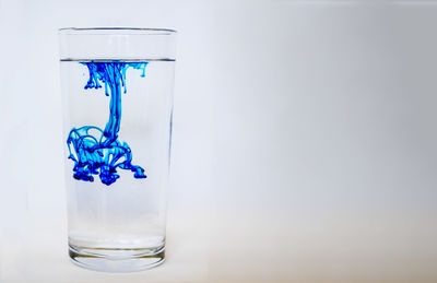 Close-up of blue glass on table against white background