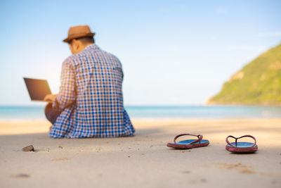 Rear view of man wearing hat at beach against sky