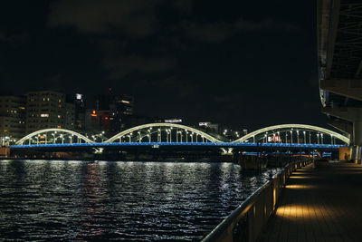 Illuminated bridge over river in city at night