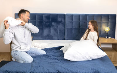 Father plays with child, dad having pillow fight with daughter in bed at family