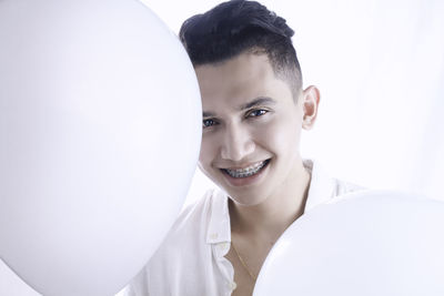 Portrait of smiling young man with balloons against white background