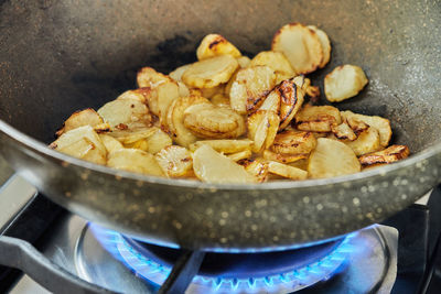 Sliced potatoes are fried in frying pan on gas stove
