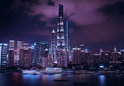 Illuminated modern buildings in city against sky at night