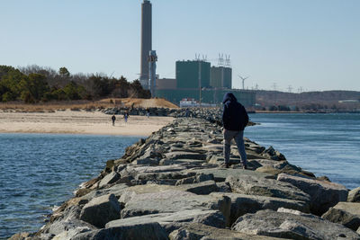 Rear view of man on rock by sea against clear sky