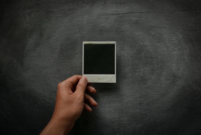 Cropped image of man hand holding instant print transfer against blackboard