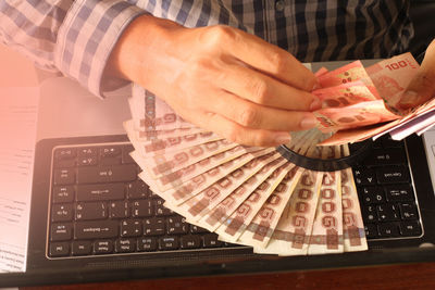 High angle view of person counting paper currency over laptop