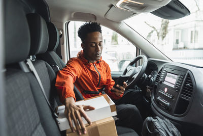 Young male driver using smart phone while sitting in delivery van