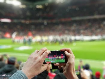 Cropped hands photographing soccer stadium through smart phone