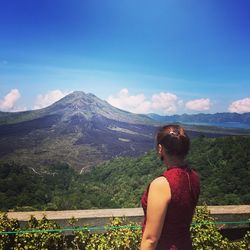 Rear view of woman standing in front of mountains against blue sky