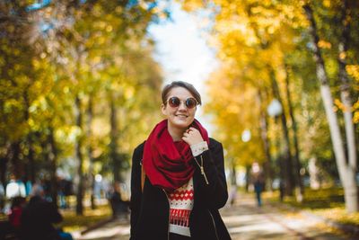 Portrait of smiling young woman standing at park during autumn