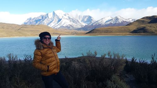 Happy woman by lake pointing at mountains during winter in torres del paine national park