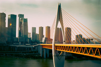 Bridge over river by buildings against sky in city