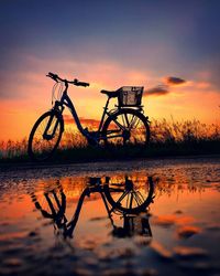 Silhouette bicycle by lake against sky during sunset