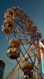 Low angle view of illuminated ferris wheel against clear blue sky at dusk