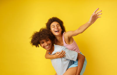 Young woman with arms raised against yellow background