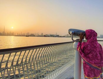 Rear view of woman photographing sea against sky during sunset