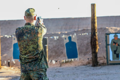 Rear view of army man shooting with handgun against wall