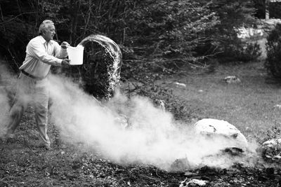 Man throwing water over land while standing against forest