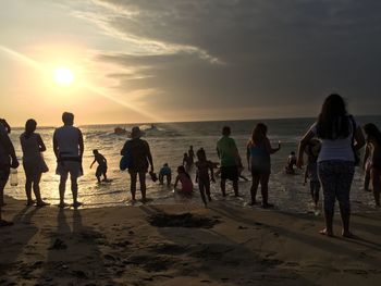 People at beach against sky during sunset