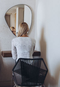 Rear view of woman sitting on chair against the mirror
