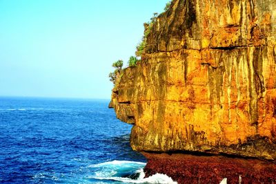 Rock formation by sea against clear blue sky